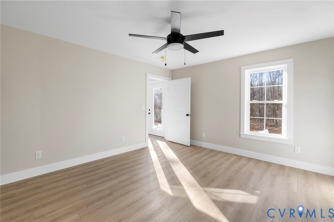 Spacious room featuring wood-finish flooring, light neutral wall tones, a modern ceiling fan, and white trim throughout