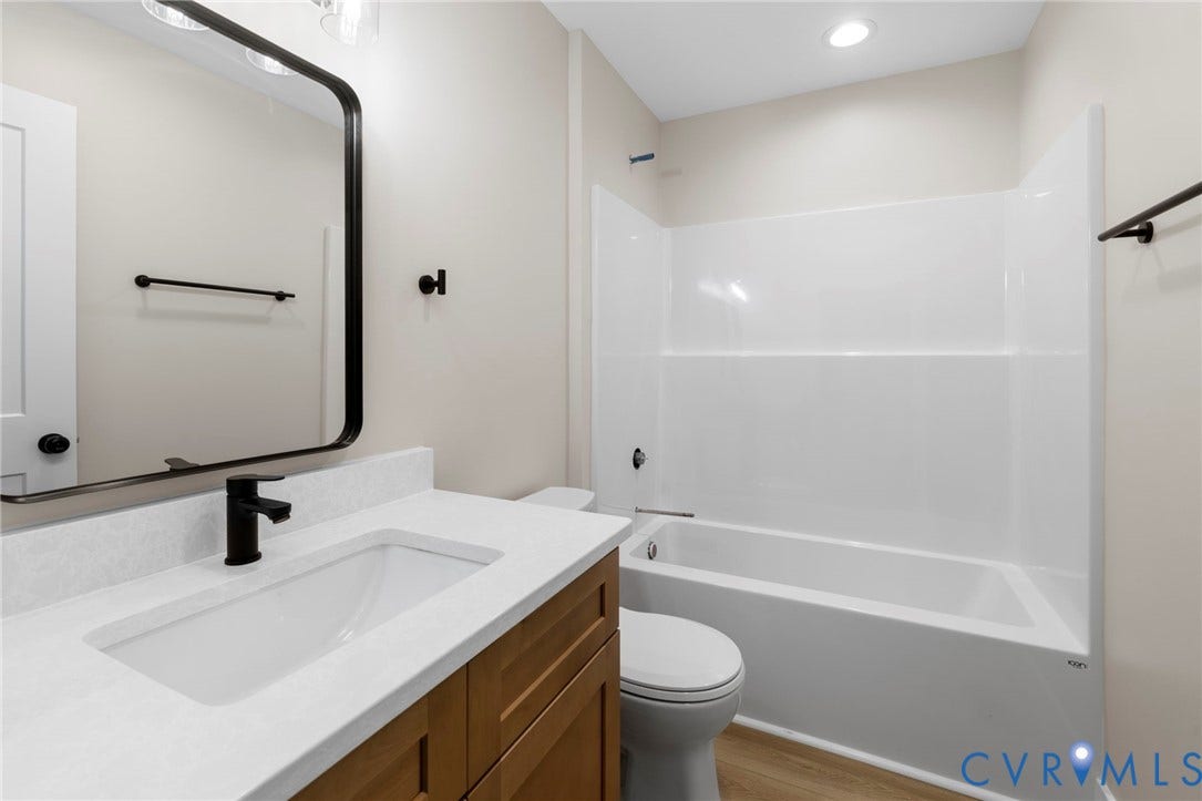 Bathroom featuring a wood-finish vanity with a white countertop, an undermount sink, and a matte black faucet