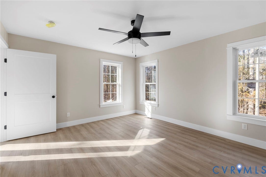 Spacious room featuring wood-finish flooring, multiple windows, a modern ceiling fan, and crisp white trim