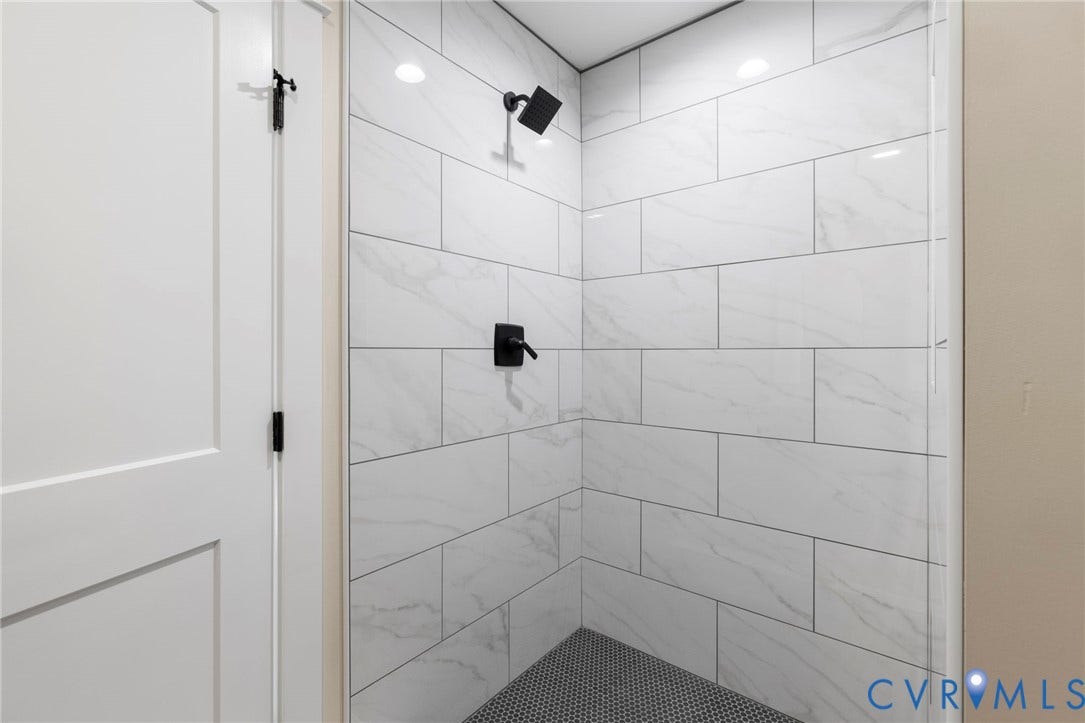 Shower stall featuring white subway-style tile walls, a black penny tile floor, and matte black fixtures