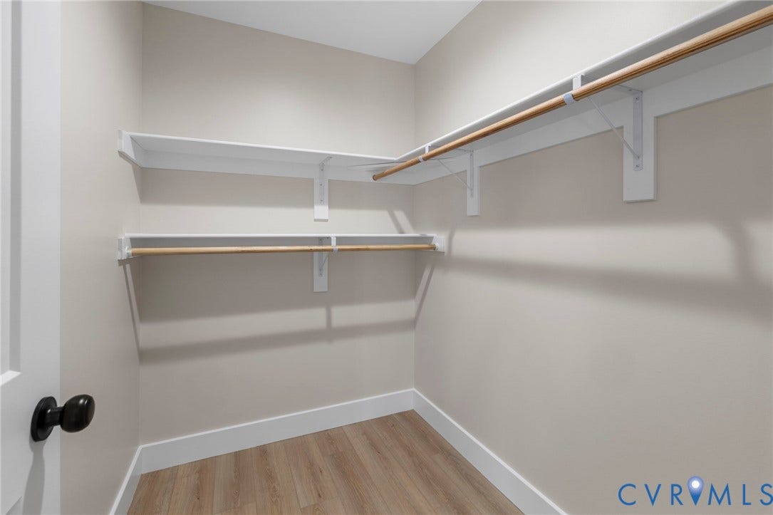 Walk-in closet featuring light wood-finish flooring, white baseboards, and built-in white shelving with wood hanging rods