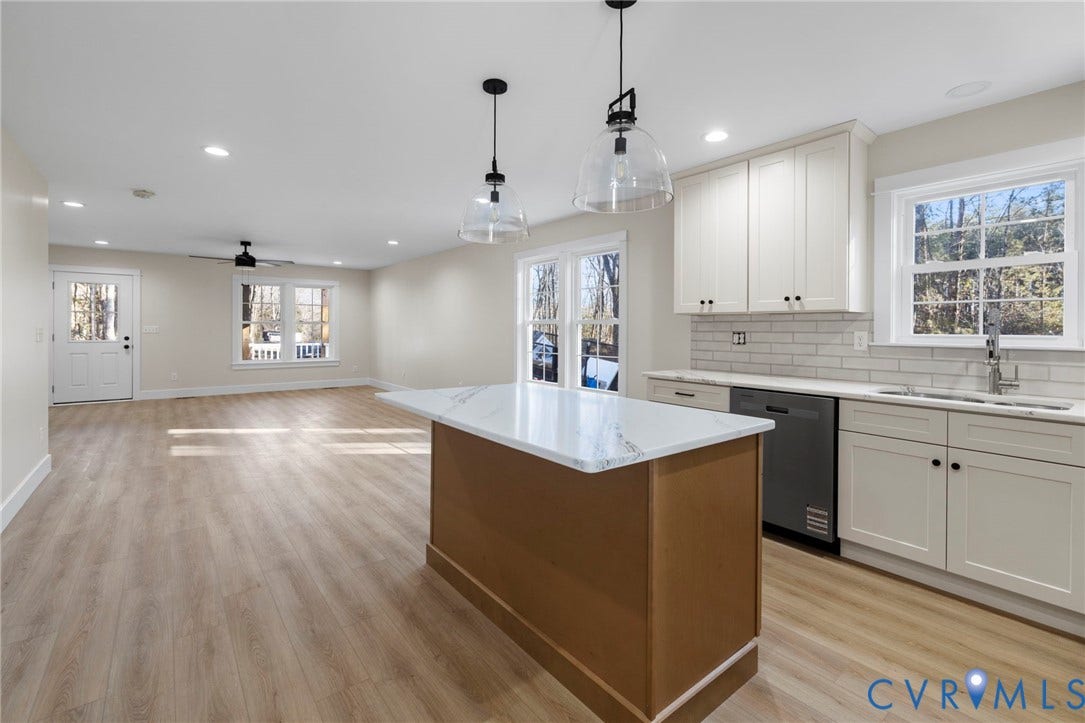 Open-concept living space featuring a central kitchen island with a white countertop, light wood-finish flooring, recessed lighting, and white cabinetry with dark hardware