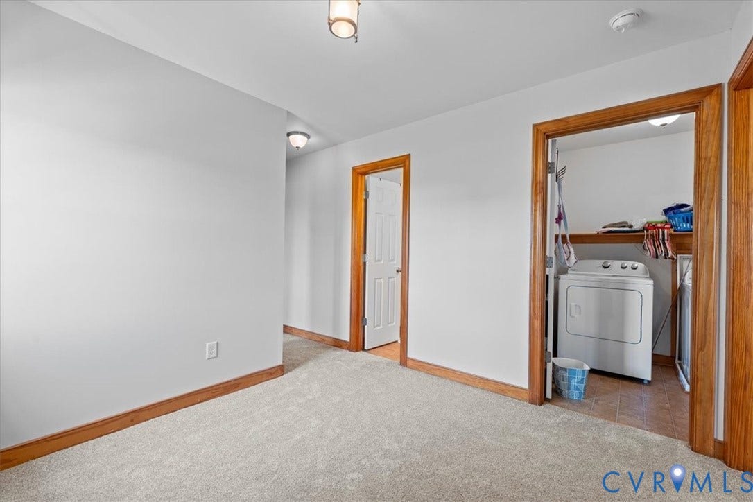 Carpeted room featuring a large window with white blinds, wood-finish trim and baseboards, and a brass-finish ceiling light fixture