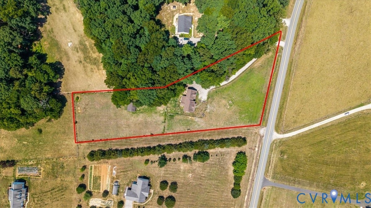 Expansive property featuring a single dwelling, mature tree lines, and open fields, bordered by paved roads