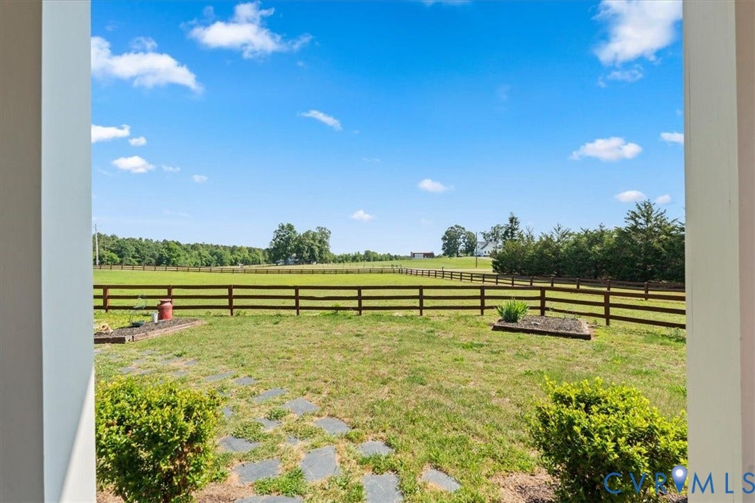 Expansive outdoor area featuring a split-rail fence, a broad grassy expanse, and established perimeter trees