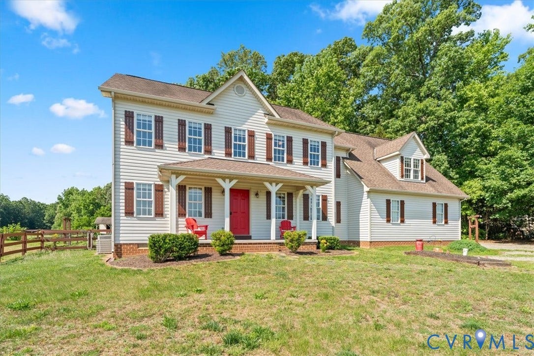 Two-story residence featuring white siding, a covered front porch with white columns, a vibrant red entry door, and brown window shutters
