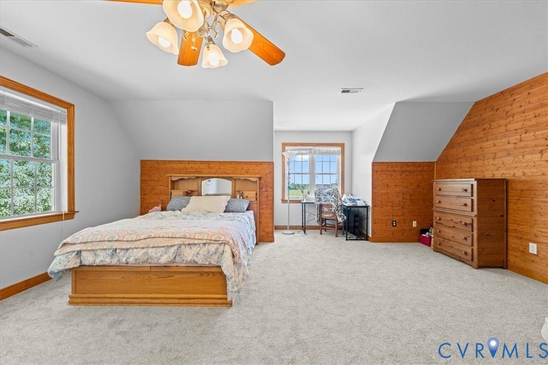 Spacious bedroom featuring light gray carpeting and white walls with a natural wood accent wall