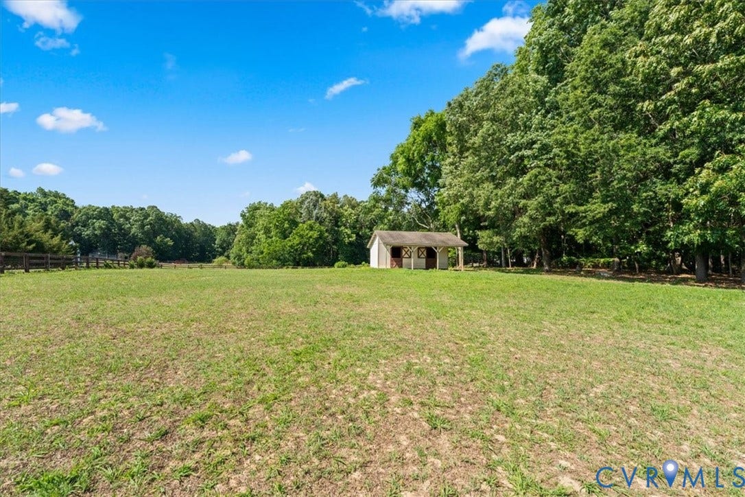 Expansive grassy field framed by mature trees, featuring a detached white outbuilding with a brown trim roof