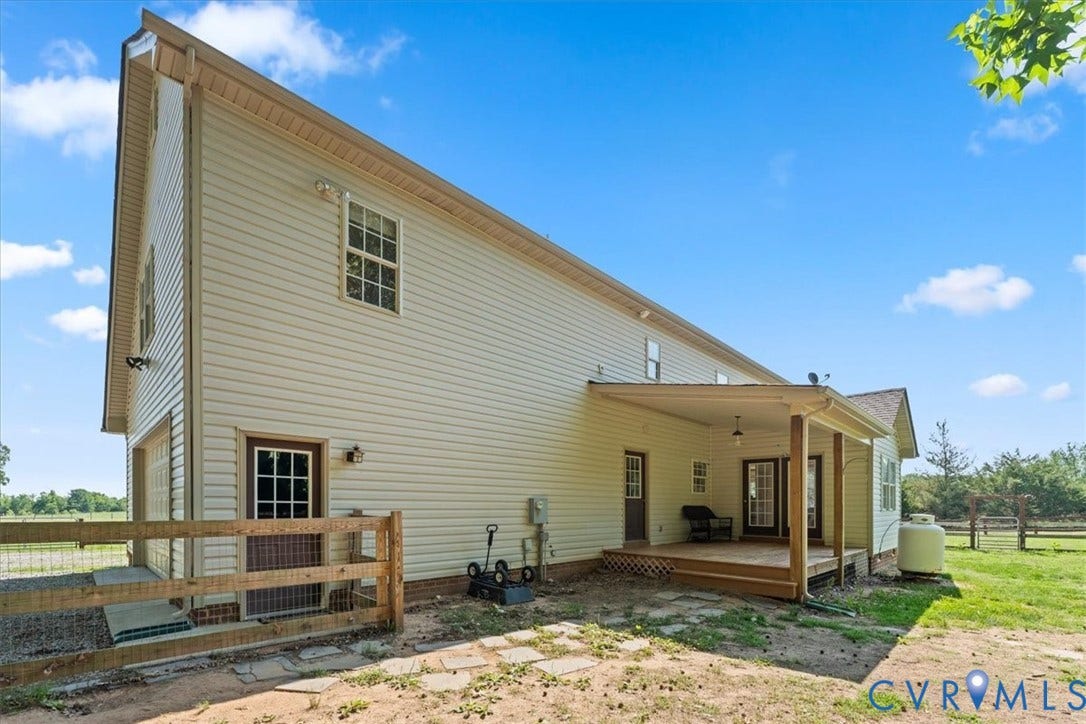 Expansive rear exterior featuring a covered wood-deck patio, white vinyl siding, multiple windows, and a partially fenced area