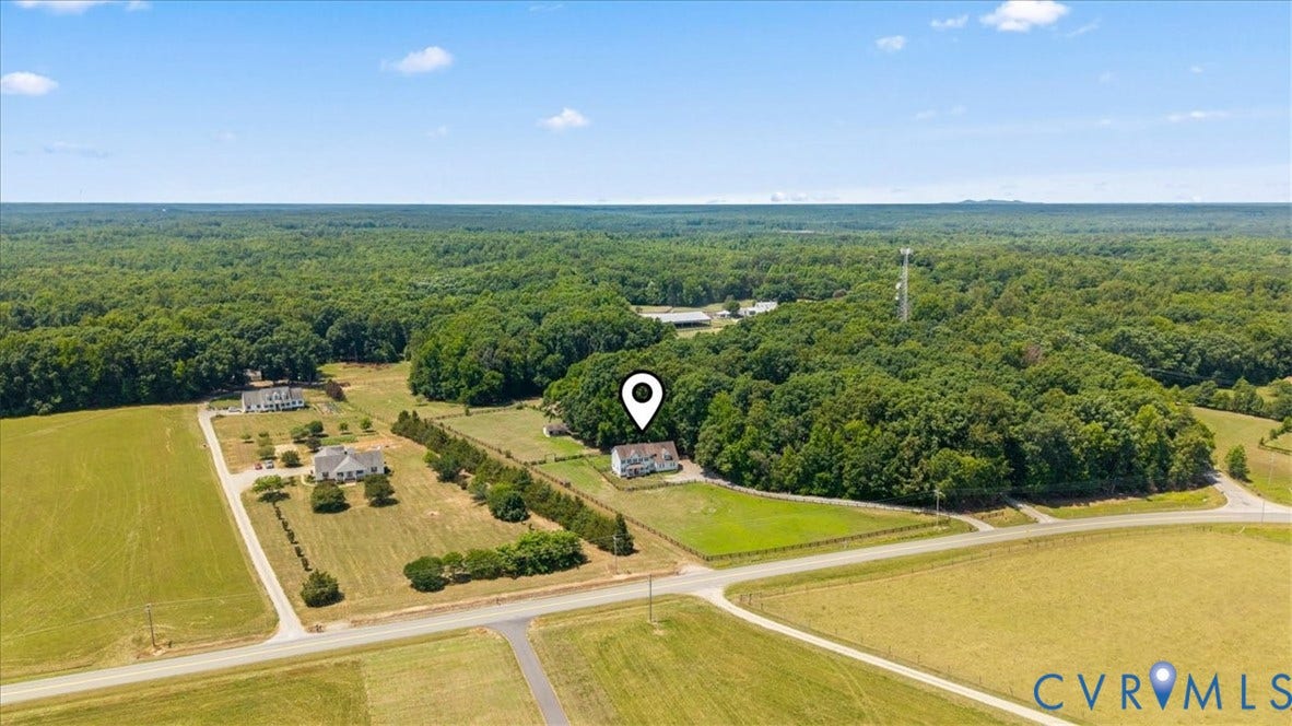 Expansive property featuring a single-family residence, mature tree line, perimeter fencing, paved road access, and surrounding open fields