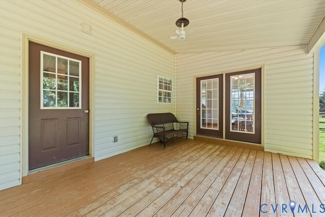 Covered wood deck featuring cream-colored siding, a brown door with a window pane, and a set of brown French doors