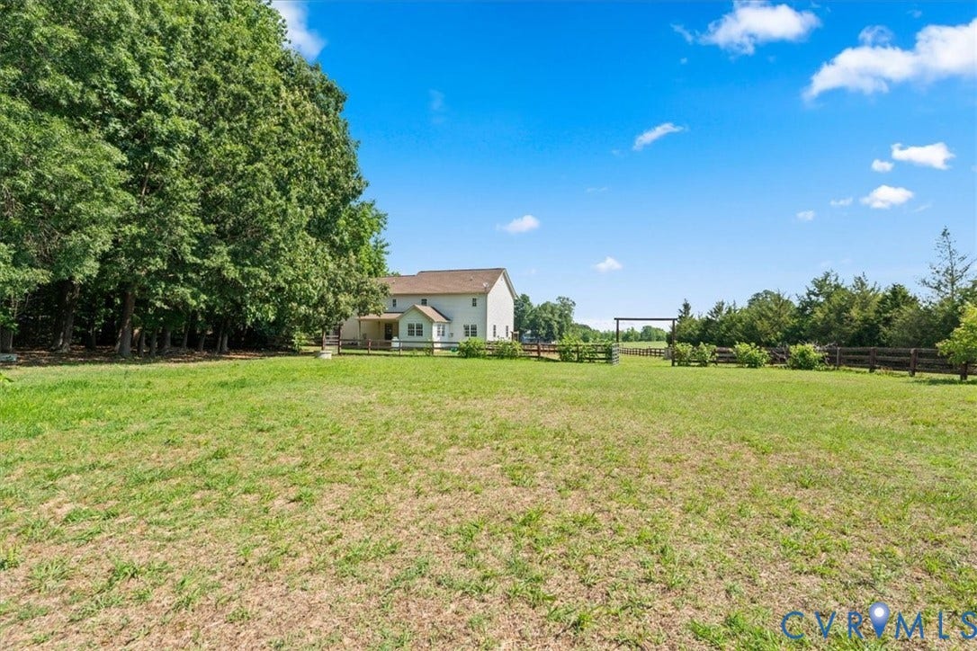 Expansive green space featuring a large residential structure, mature perimeter trees, and a distant wooden fence line