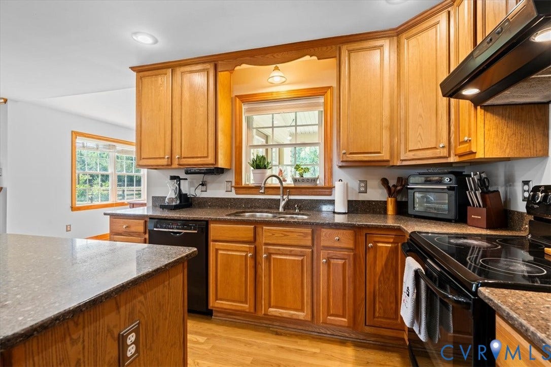 Kitchen featuring wood-finish flooring, a central island, recessed lighting, wood cabinetry, and dark-toned countertops