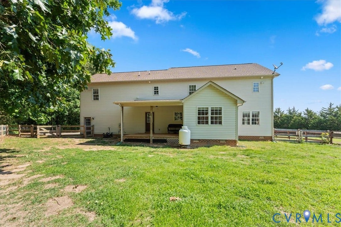 Rear exterior featuring a covered porch with wood decking, an additional ground-level extension, multiple windows, and a fenced perimeter