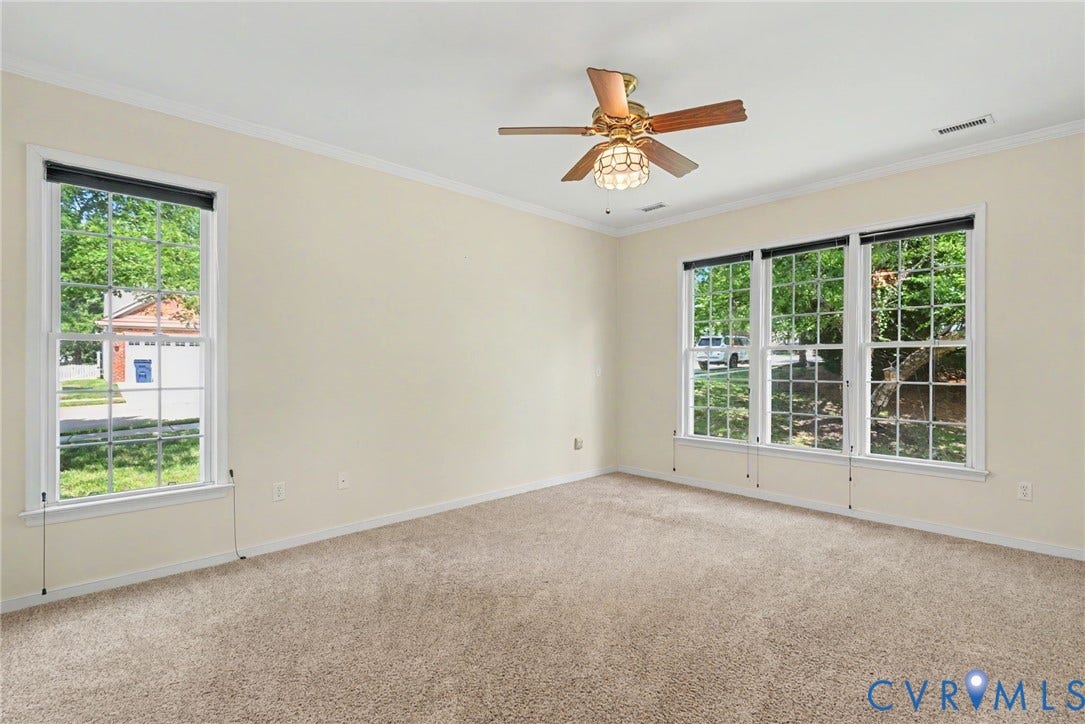 Carpeted room with a ceiling fan, crown molding, and multiple windows featuring grid patterns