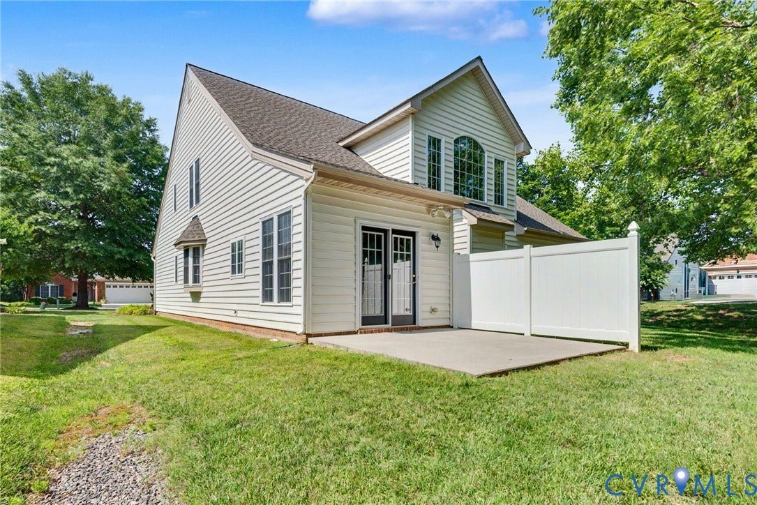 Rear exterior featuring a concrete patio, white vinyl privacy fencing, and sliding glass doors