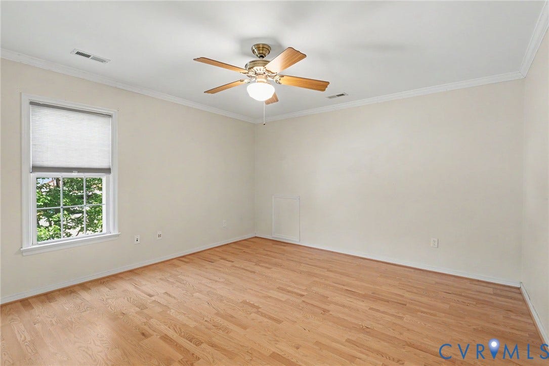 Spacious room featuring wood-finish flooring, a ceiling fan with light fixture, window with roller shade, and crown molding