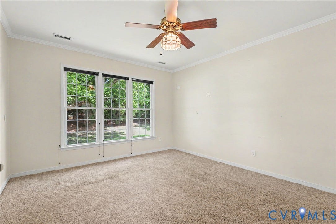Carpeted room featuring a three-panel window overlooking mature trees, crown molding, and a ceiling fan with light fixture