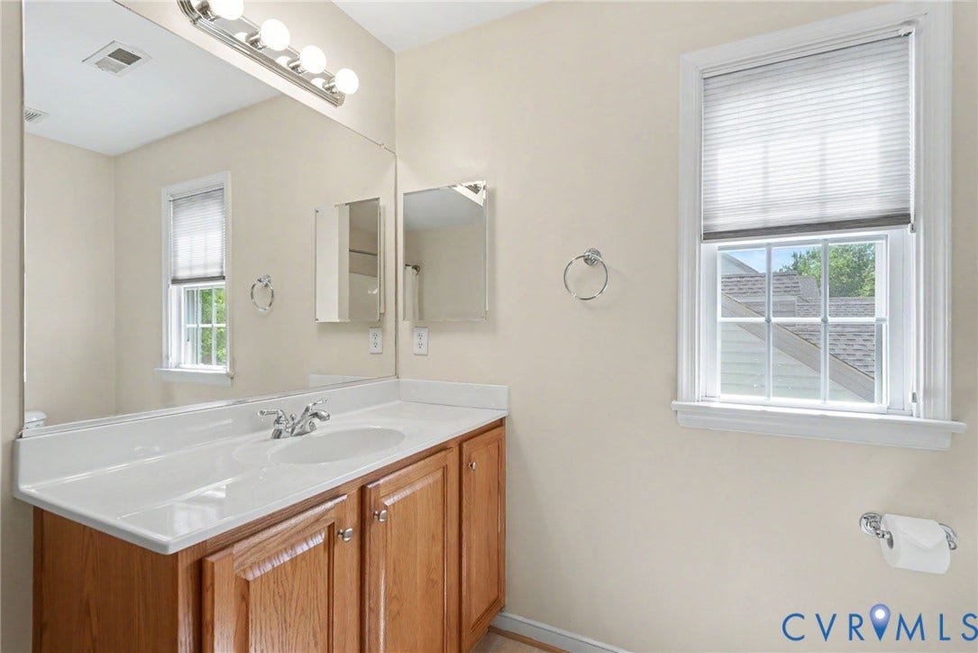 Bathroom vanity featuring a light wood-finish cabinet with silver hardware, an integrated white sink, and a chrome faucet