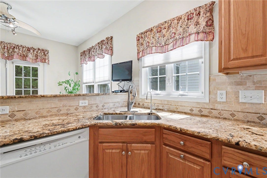 Kitchen featuring granite countertops, wood cabinetry, a double basin stainless steel sink with a gooseneck faucet, a tile backsplash with decorative accents, and a built-in dishwasher