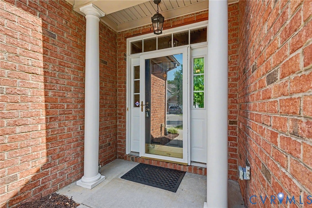 Brick facade entry featuring a full-light storm door, white main entry door, transom window, and architectural columns