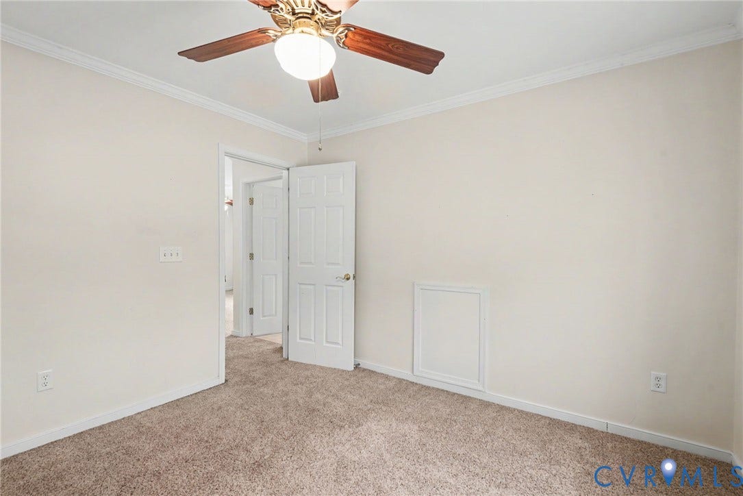 Neutral-toned room featuring a ceiling fan with wood-finish blades, white crown molding, and brown carpet flooring