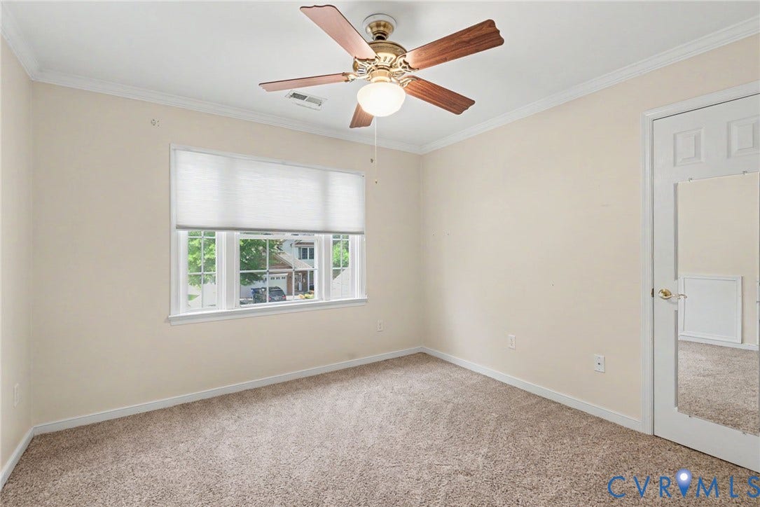 Carpeted room featuring a white-framed window with blinds, crown molding, and a ceiling fan with wood-finish blades