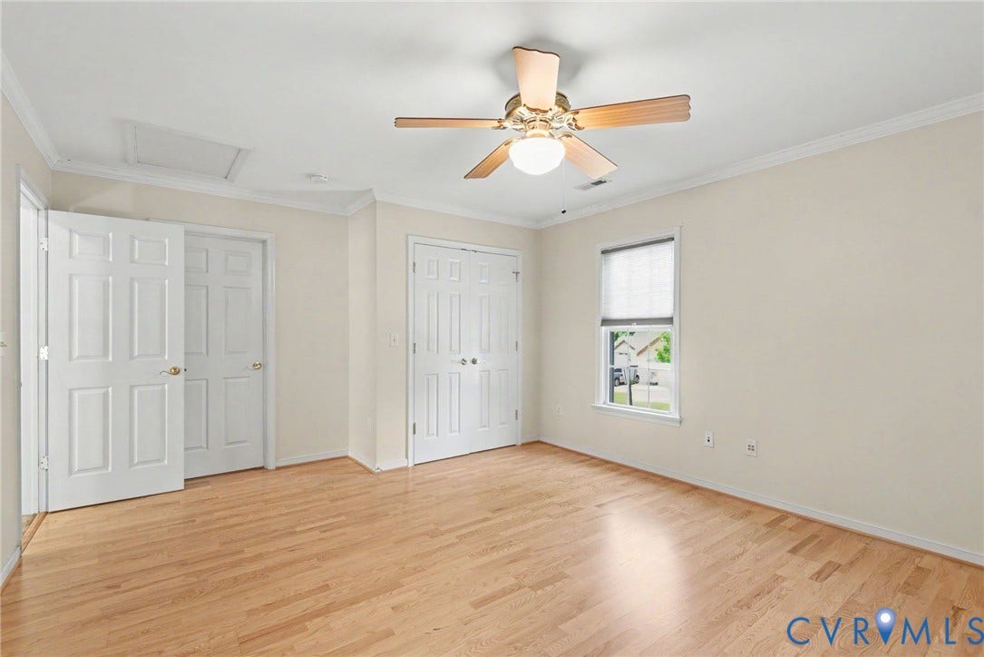 Spacious room featuring wood-finish flooring, white paneled doors, crown molding, and a ceiling fan with integrated lighting