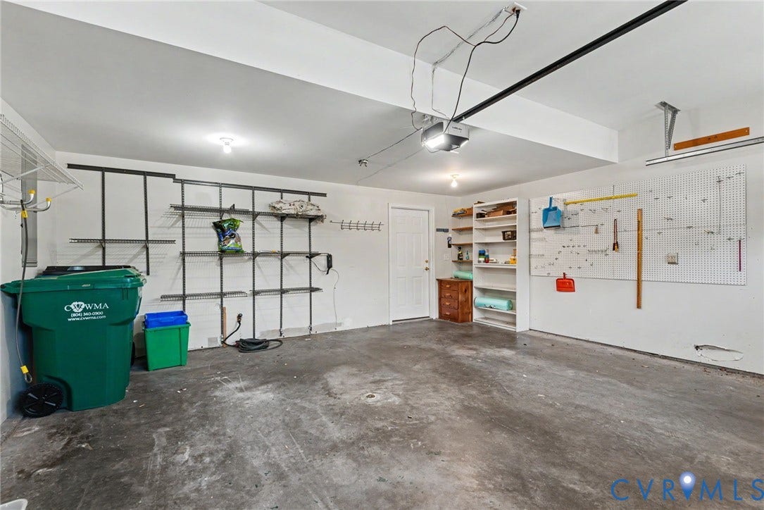 Spacious garage featuring concrete flooring, built-in shelving, a white side door, and a garage door opener