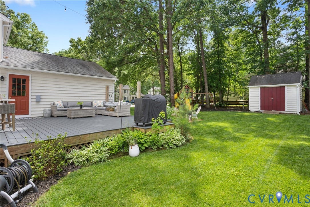 10100 Contessa Court, Glen Allen, VA 23060 Expansive backyard featuring a gray composite deck, lush green lawn, mature trees, and a white storage shed with red doors