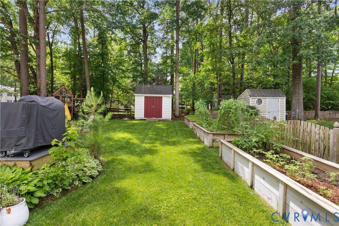 10100 Contessa Court, Glen Allen, VA 23060 Expansive backyard featuring a green lawn, two storage sheds, a wooden privacy fence, and raised garden beds