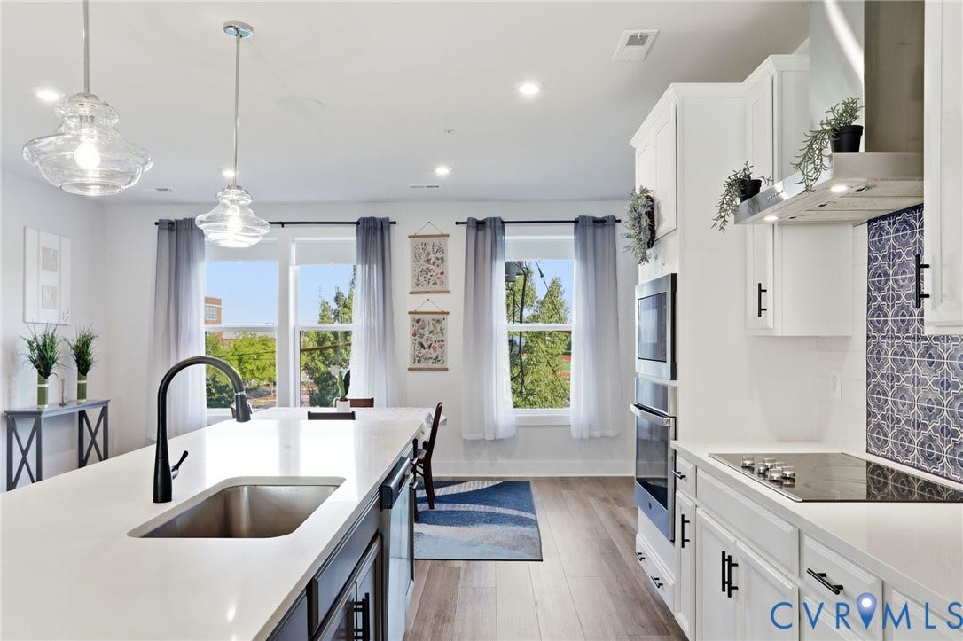 1121 N Lombardy Street, #B, Carver Square, Richmond, VA 23220 Modern kitchen featuring an expansive island with an undermount sink and matte black faucet, pendant lighting, white cabinetry with black hardware, an integrated cooktop with a stainless steel range hood, and a blue and white patterned tile backsplash