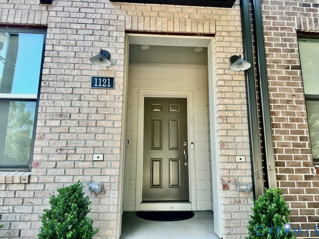 1121 N Lombardy Street, #B, Carver Square, Richmond, VA 23220 Brick facade entry featuring a paneled door, recessed lighting, and two wall-mounted fixtures