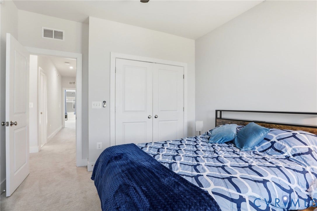 1121 N Lombardy Street, #B, Carver Square, Richmond, VA 23220 Bedroom featuring light gray wall paint, light-colored carpet, white bi-fold closet doors with brushed nickel hardware, and an open doorway revealing a hallway