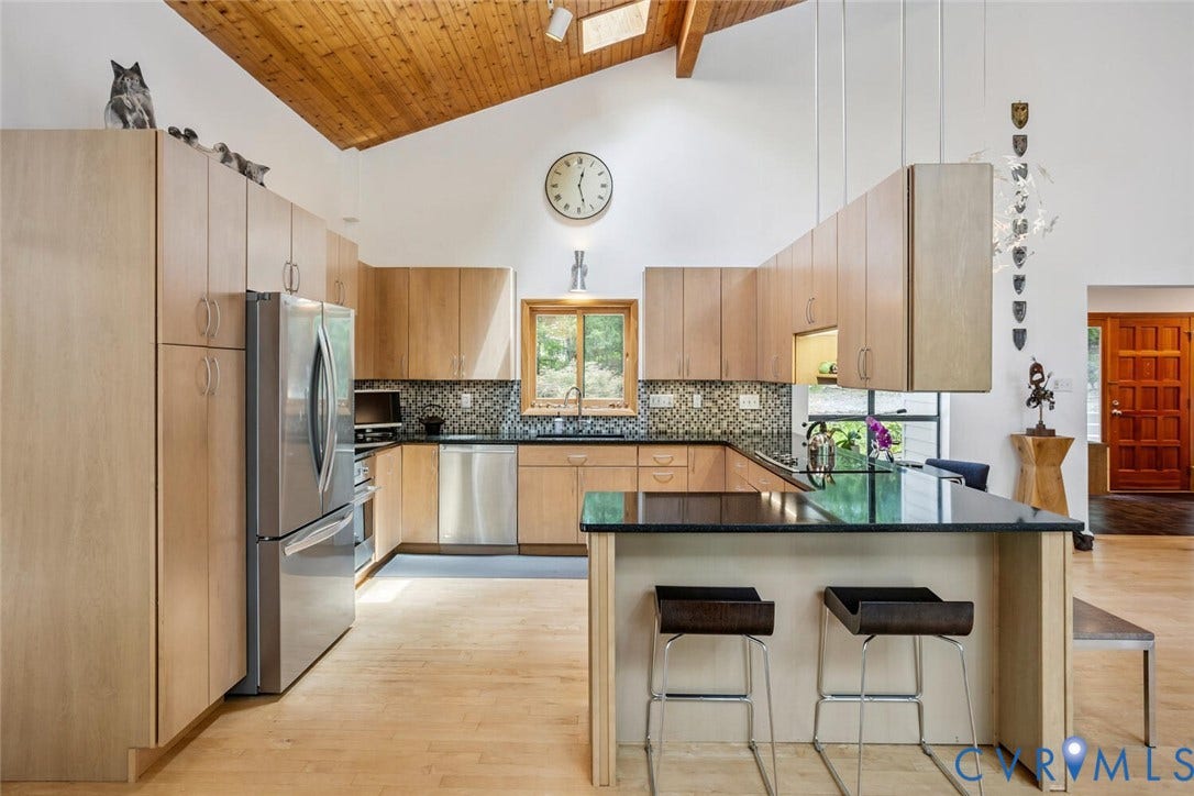 1474 Timber Ridge, Maidens, VA 23102 Modern kitchen featuring light wood-finish cabinetry, stainless steel appliances, a black countertop island with seating, a mosaic tile backsplash, and wood-finish flooring