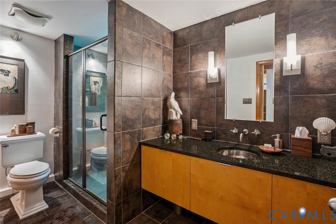 1474 Timber Ridge, Maidens, VA 23102 Bathroom featuring dark-toned tiled walls and flooring, a glass-enclosed shower, a light wood-finish vanity with an undermount sink, and a black speckled countertop