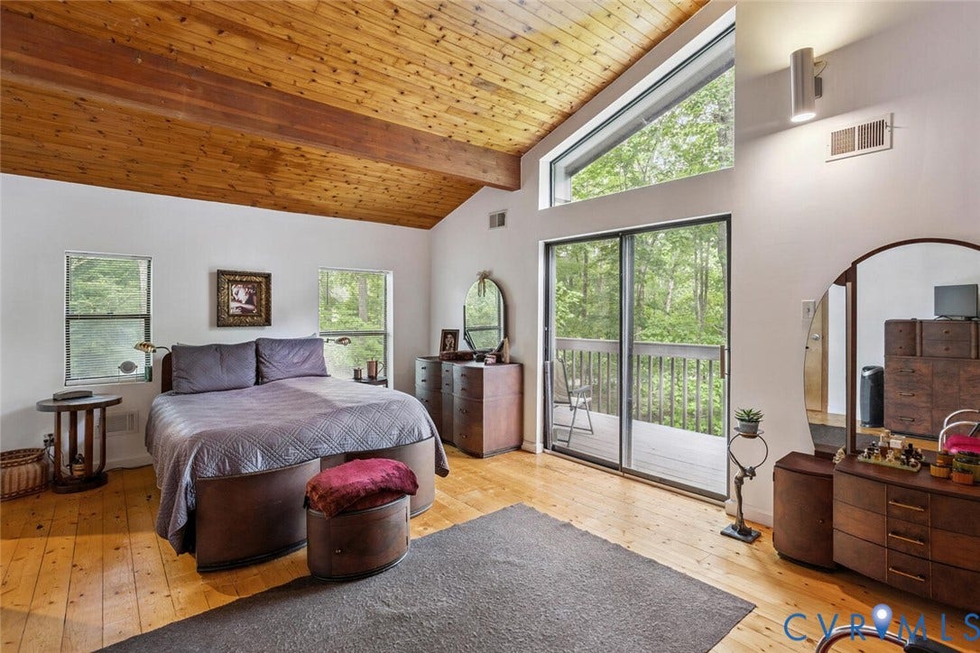 1474 Timber Ridge, Maidens, VA 23102 Second floor primary with balcony access. Vaulted wood-plank ceiling with exposed beams, wood-finish flooring, white walls, sliding glass door to exterior decking, and an upper transom window