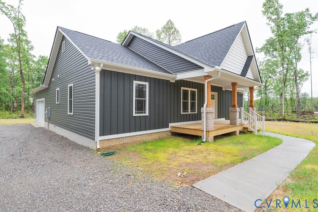 1220 Jefferson Highway, Moseley Estates, Louisa, VA 23093 Contemporary exterior featuring dark gray vertical and horizontal siding, a covered front porch with wood columns and brick bases, a gravel driveway, and a concrete walkway