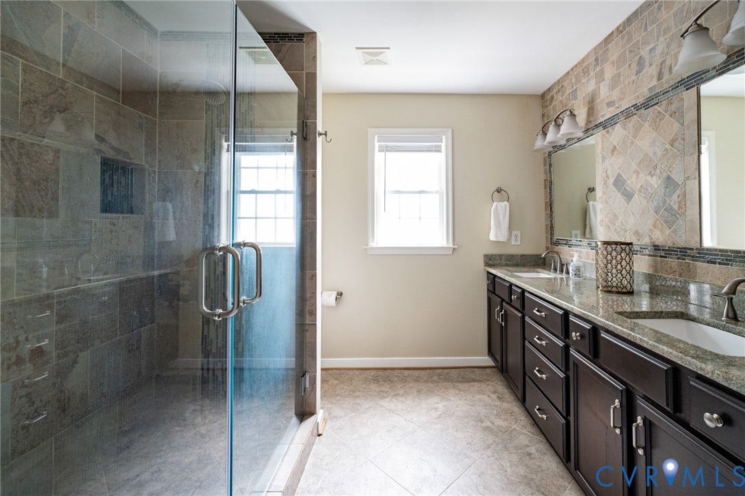 10517 Park Tree Place, Mountain Glen/ Glen Allen, Glen Allen, VA 23060 Spacious bathroom featuring a glass-enclosed shower with tile surround and integrated niche, a long dark-wood vanity with dual integrated sinks and stone-finish countertop, and decorative wall tiling
