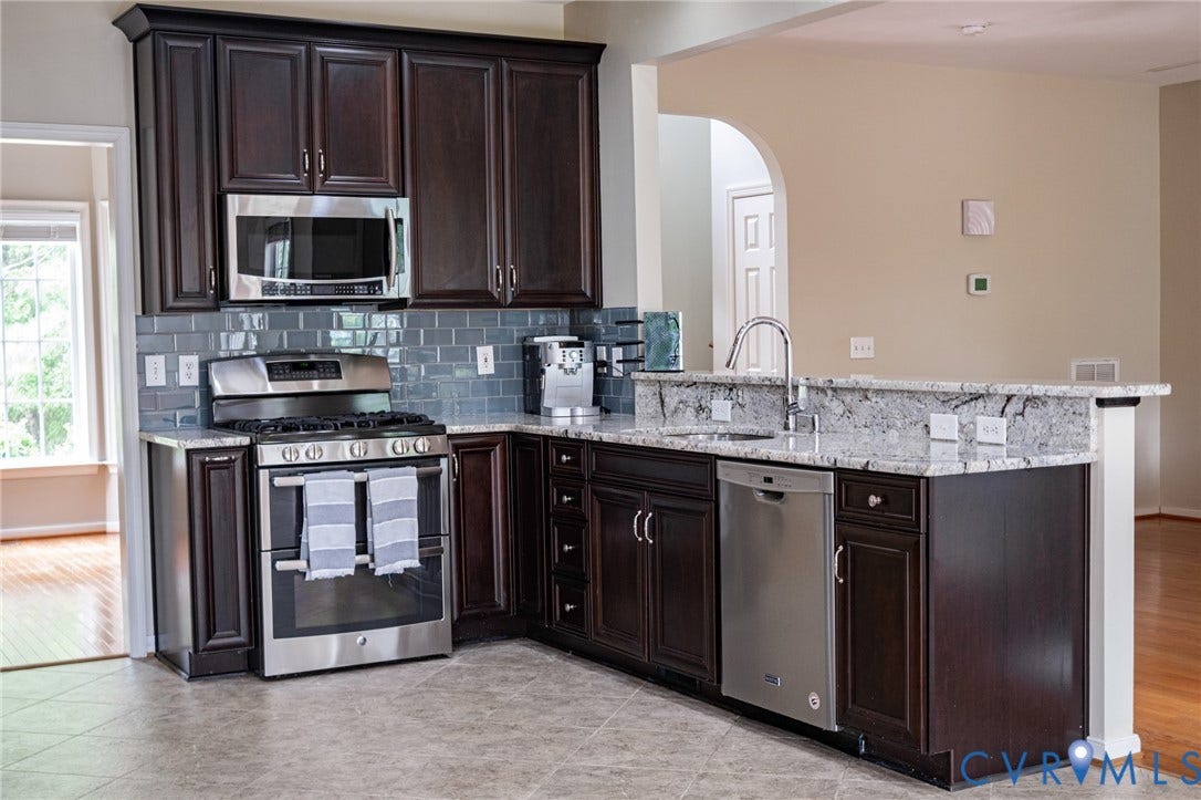 10517 Park Tree Place, Mountain Glen/ Glen Allen, Glen Allen, VA 23060 Kitchen featuring dark wood cabinetry, stainless steel appliances, a tile backsplash, light-toned countertops, and a built-in sink with a gooseneck faucet
