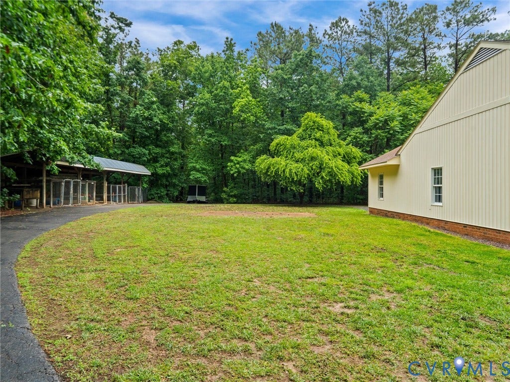 3420 Goodwyn Road, Powhatan, VA 23139 Expansive grassy yard with mature trees, a paved driveway, and a covered outbuilding featuring multiple partitioned enclosures