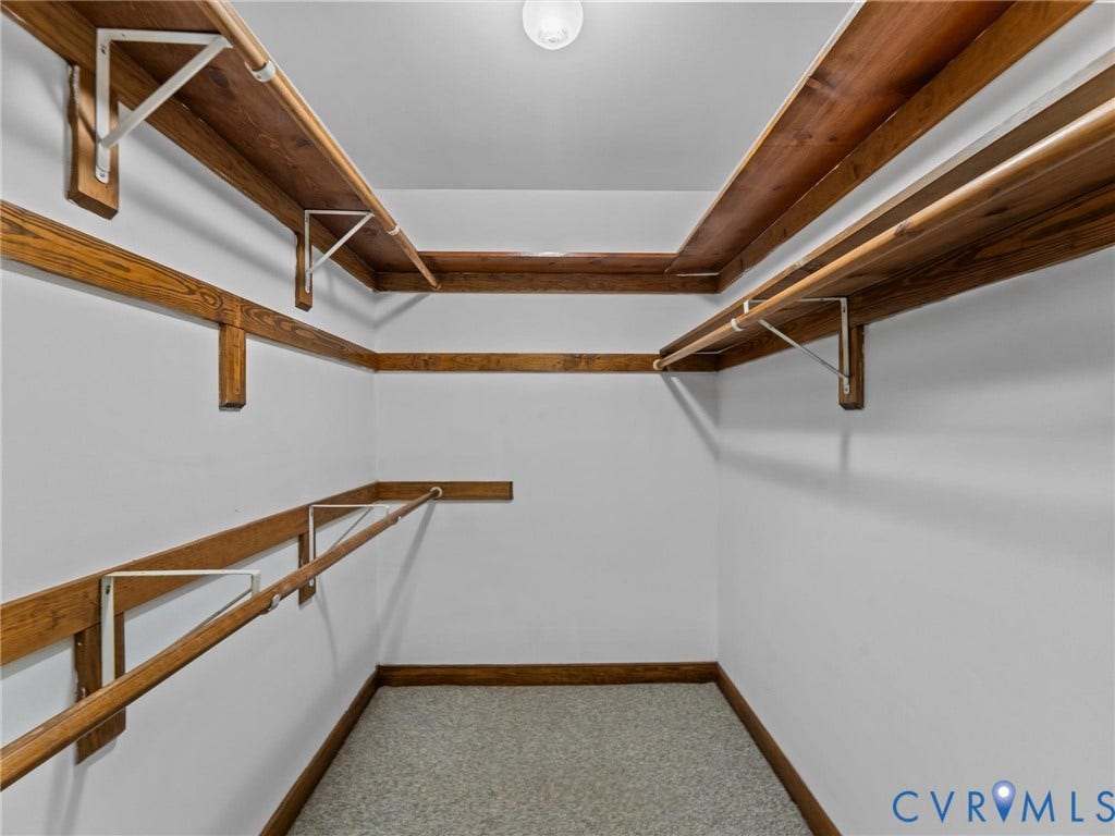 3420 Goodwyn Road, Powhatan, VA 23139 Walk-in closet featuring extensive wood-finish shelving, multiple hanging rods, durable carpet flooring, and a ceiling-mounted light fixture