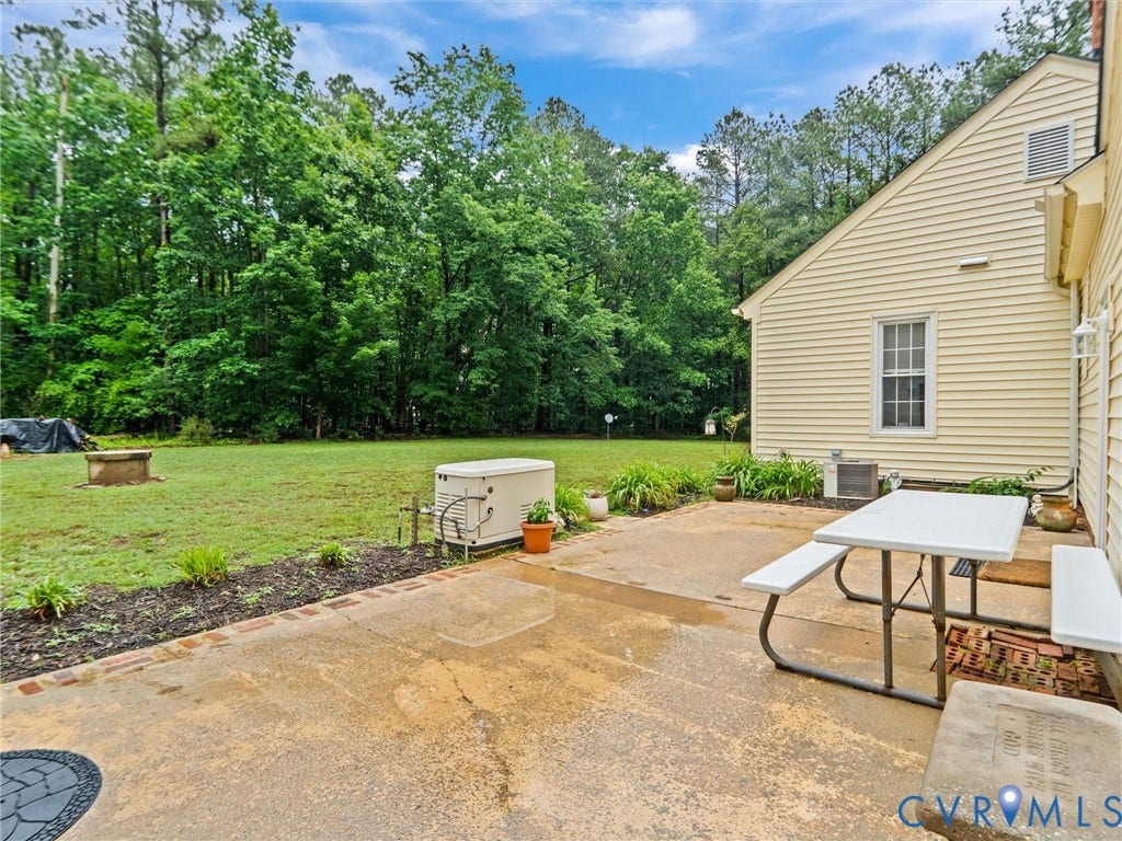 3420 Goodwyn Road, Powhatan, VA 23139 Expansive green space featuring a concrete patio with brick edging, a built-in fire pit, mature trees, and a permanent generator