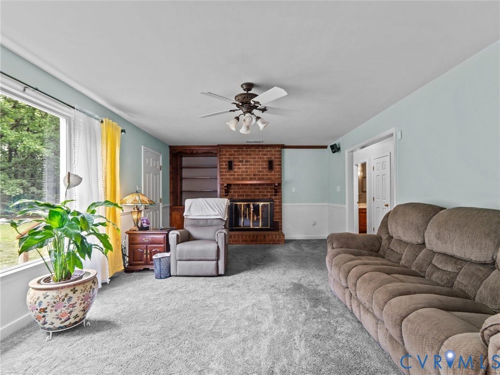 3420 Goodwyn Road, Powhatan, VA 23139 Living area featuring a brick fireplace with built-in shelving, light-colored walls, and gray carpeting. Hardwoods underneath.