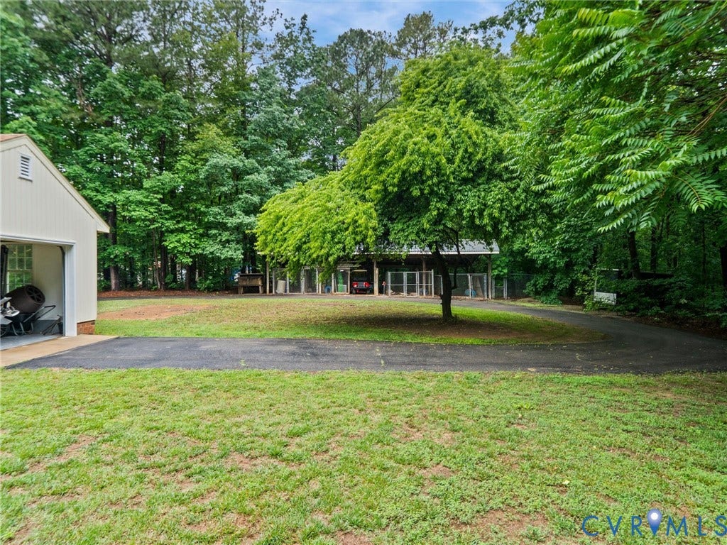 3420 Goodwyn Road, Powhatan, VA 23139 Expansive grassy area featuring a paved driveway, mature trees, and a detached outbuilding with a single garage door