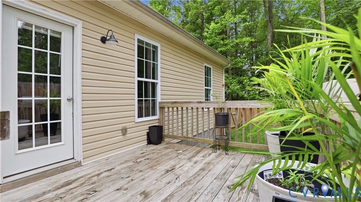 2406 Emanuel Church Road, Powhatan, VA 23139 Wood deck featuring a white paneled door with grid-patterned glass, a single-hung window with white trim, tan horizontal siding, and a black gooseneck outdoor light fixture