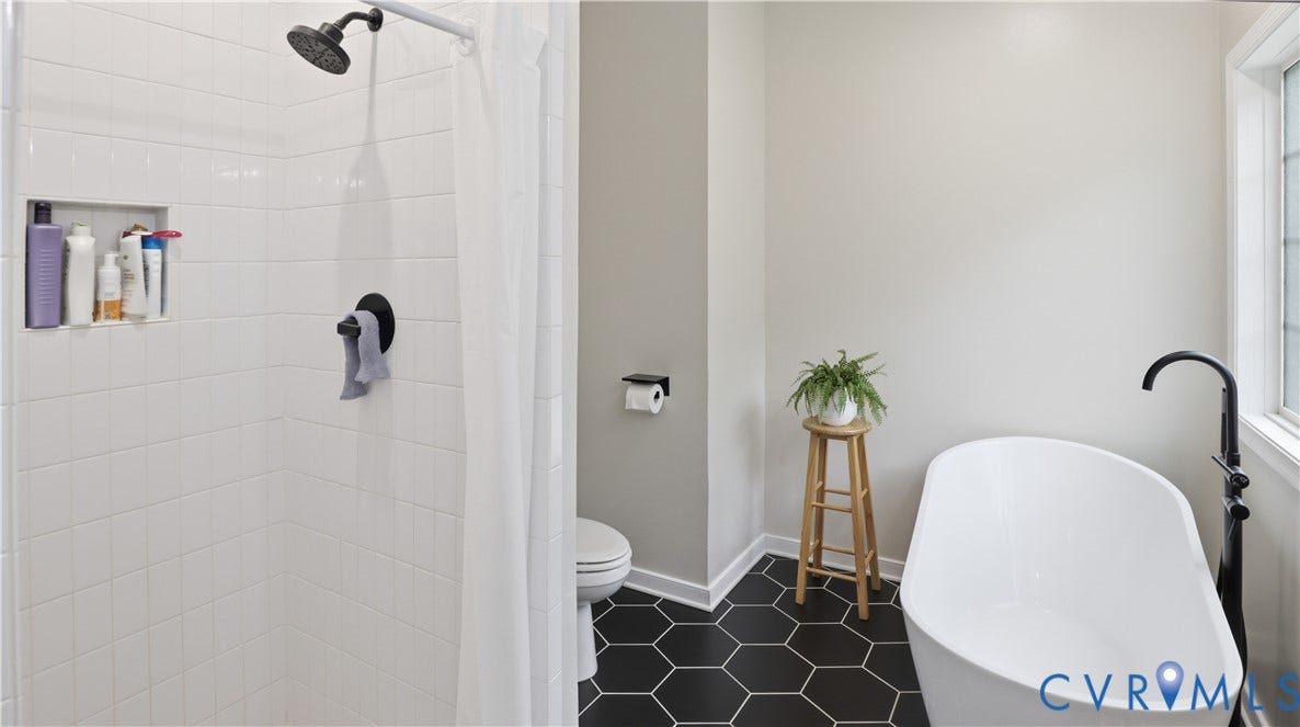 2406 Emanuel Church Road, Powhatan, VA 23139 Bathroom featuring a freestanding soaking tub, black hexagonal floor tiling, a white tiled shower with a built-in niche, and a window providing natural light