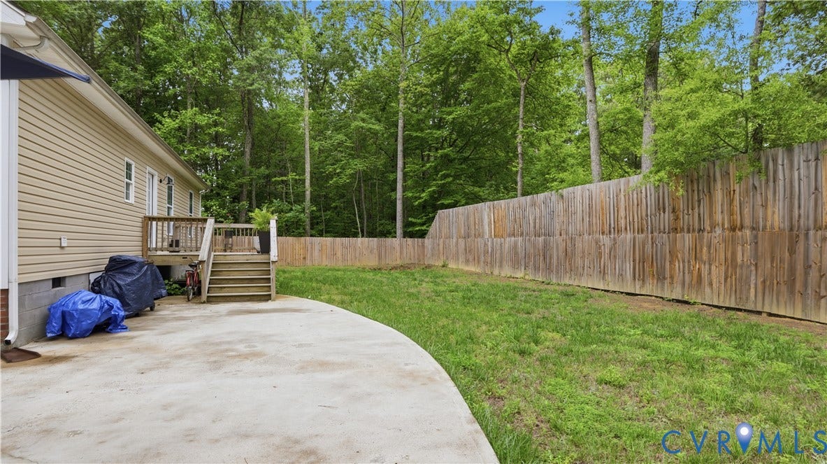 2406 Emanuel Church Road, Powhatan, VA 23139 Expansive backyard featuring a concrete patio, wooden deck with stairs, a full privacy fence, and mature trees providing a natural perimeter