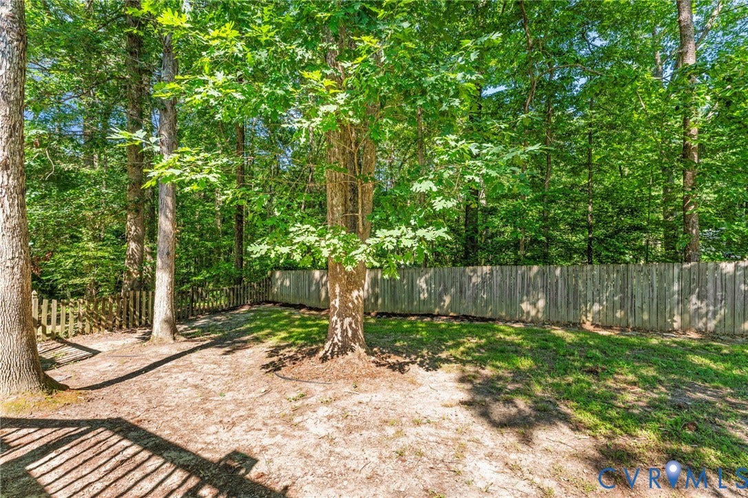 3020 Sand Hills Drive, Chester, VA 23831 Wooded backyard featuring mature trees, a wooden privacy fence, and a partial picket fence