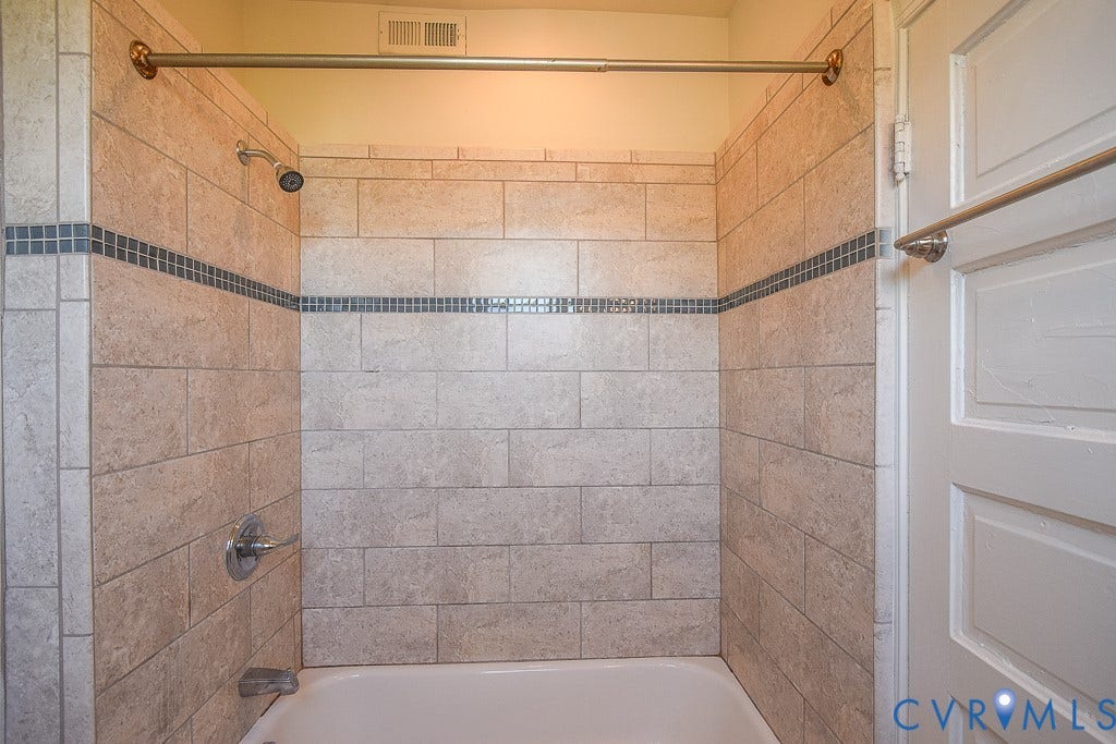 120 S Arthur Ashe Boulevard, #1, Richmond, VA 23220 Bathtub and shower combination featuring neutral-toned rectangular wall tiles, a decorative mosaic tile accent band, a polished chrome shower head, and coordinating faucet hardware